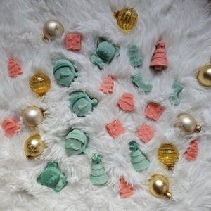 Dišeči vosek Black Pine & Cinnamon v mehkih zimskih tonih, obdan z borovimi vejicami in cimetovimi palčkami – prazničen vonj doma in topline.